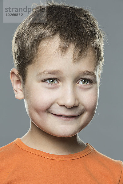 Lächelnder Junge schaut weg vor grauem Hintergrund
