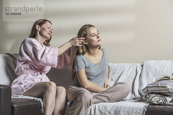 Mutter macht die Haare der Tochter auf dem Sofa zu Hause