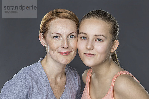 Porträt von lächelnder Mutter und Tochter vor grauem Hintergrund