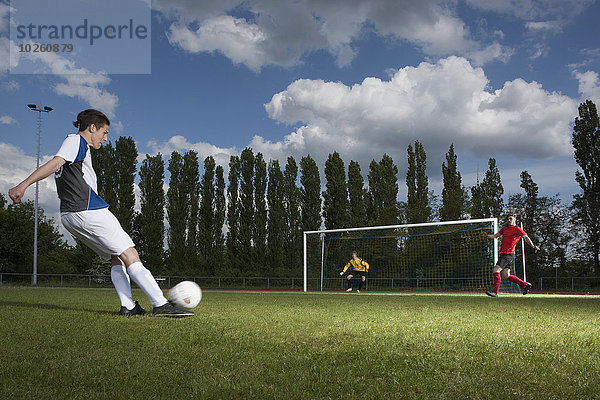 Volle Länge des jungen Fußballspielers  der den Ball in Richtung Torpfosten kickt.