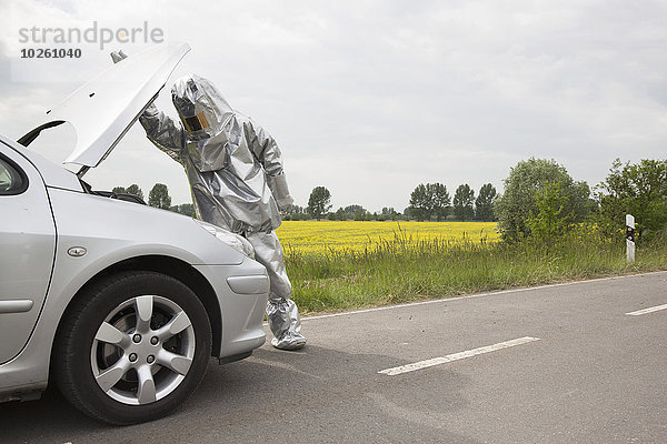 Eine Person in einem Strahlenschutzanzug  die unter die Motorhaube eines Autos schaut.