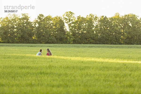 Fernbild von Mädchen  die auf einem grasbewachsenen Feld sitzen.