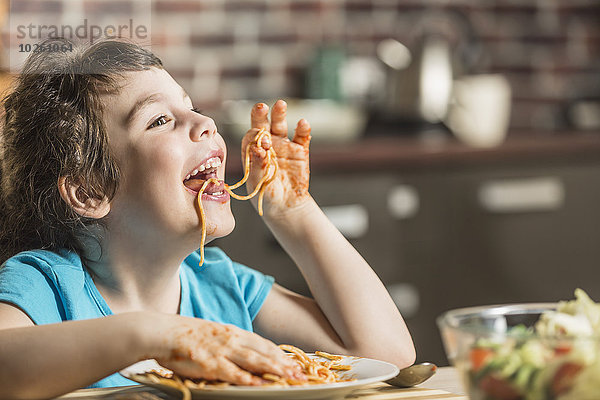 Fröhliches kleines Mädchen  das zu Hause Spaghetti mit den Händen isst.