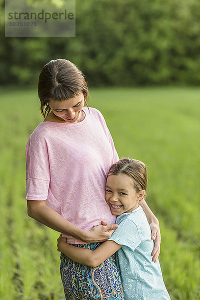 Lächelndes Mädchen umarmt Mutter auf dem Feld