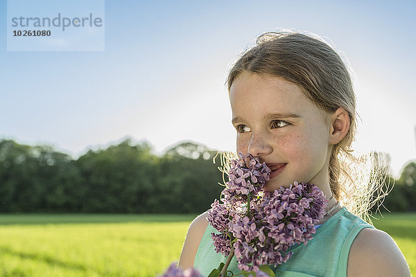 Glückliches Mädchen riecht lila Blumen auf dem Feld