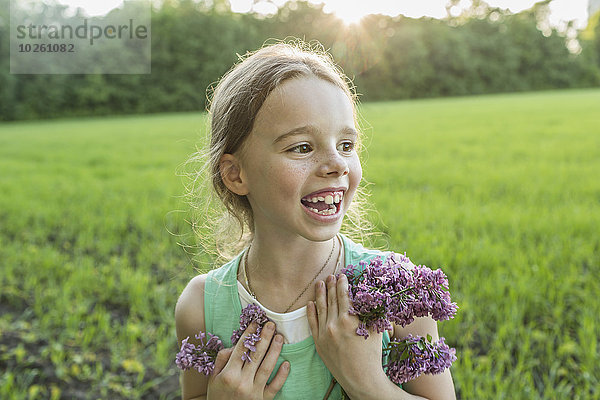 Fröhliches Mädchen mit lila Blumen auf dem Feld