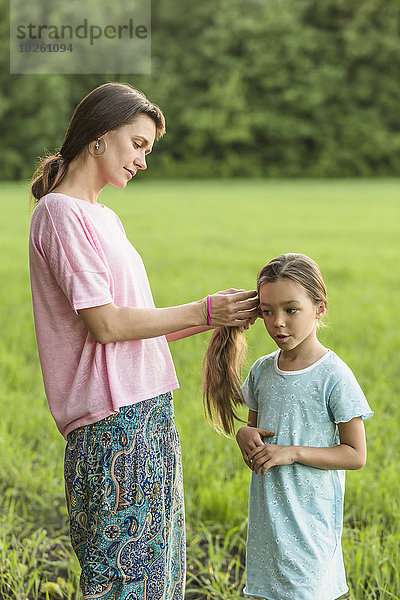 Mutter macht die Haare der Tochter auf dem Feld