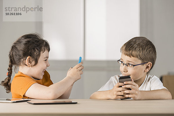 Lächelnde Schwester beim Fotografieren des Bruders per Handy zu Hause