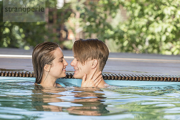 Seitenansicht eines leidenschaftlichen Paares  das im Schwimmbad lächelt.