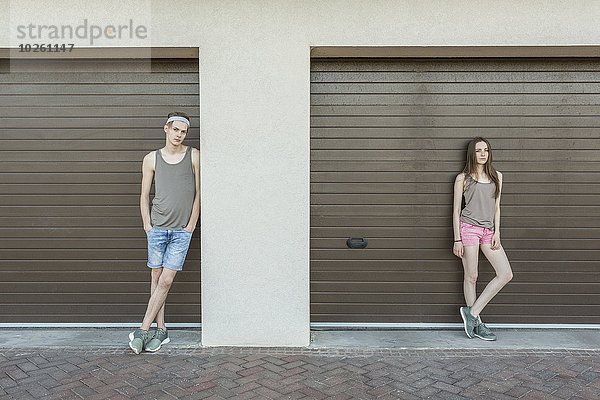 Junger Mann und Frau  die sich gegen eine geschlossene Garage lehnen.