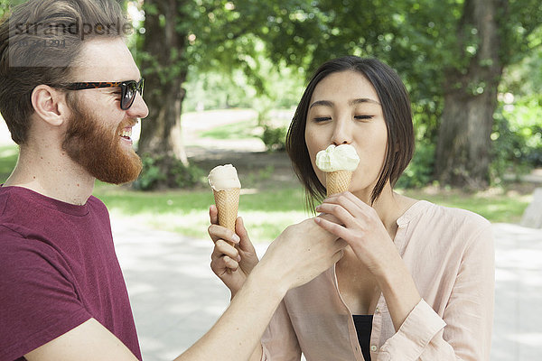 Glücklicher Mann füttert Frau im Park mit Eiscreme