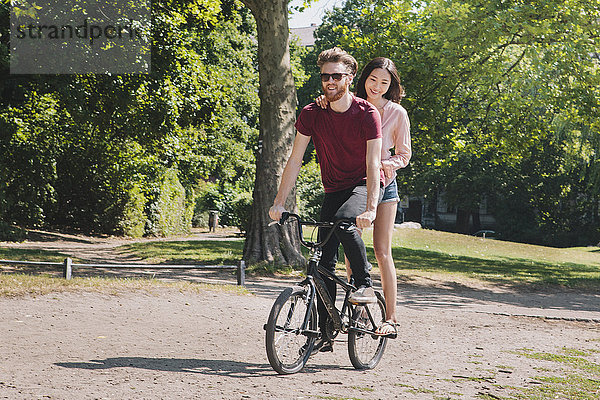 Volle Länge des jungen Paares beim Fahrradfahren im Park