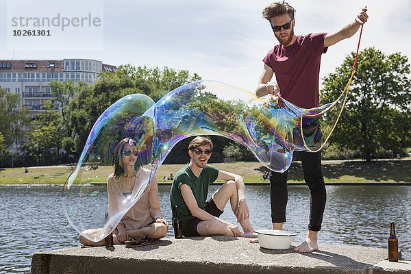 Glückliche Freunde genießen mit großer Blase an der Stützmauer am Kanal im Park