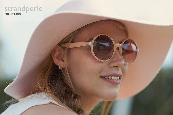 Porträt einer jungen Frau mit Sonnenbrille und Hut im Park