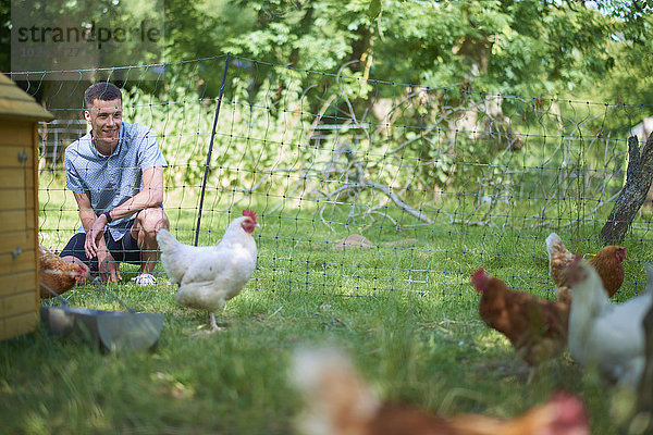 Glücklicher junger Mann schaut auf Huhn im Park