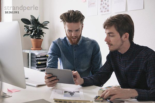 Junge Geschäftsleute  die gemeinsam am Schreibtisch ein digitales Tablett benutzen