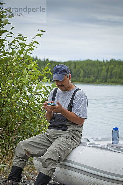 Wasserrand sitzend benutzen Mann Sommer Boot Fluss vorwärts Smartphone Kenai-Fjords-Nationalpark Alaska Ethnisches Erscheinungsbild Gummi