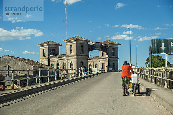 zwischen inmitten mitten hoch oben Mann schieben Fernverkehrsstraße Fahrrad Rad Grenze Brasilien Uruguay