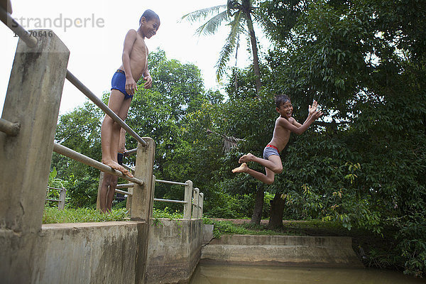 Kinder  die von einem Zaun ins Wasser springen; Battambang  Kambodscha