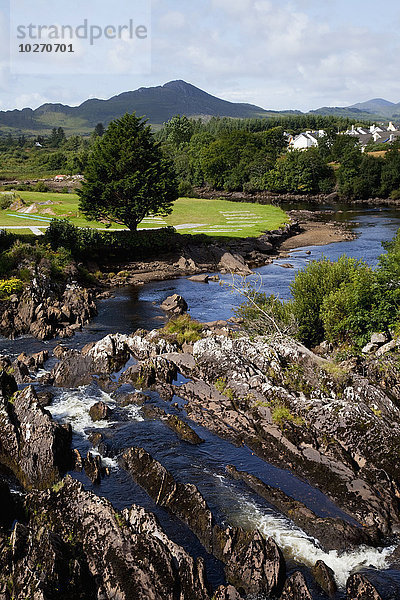 Ein über Felsen fließender Fluss und eine üppige Landschaft mit Häusern; Sneem  County Kerry  Irland
