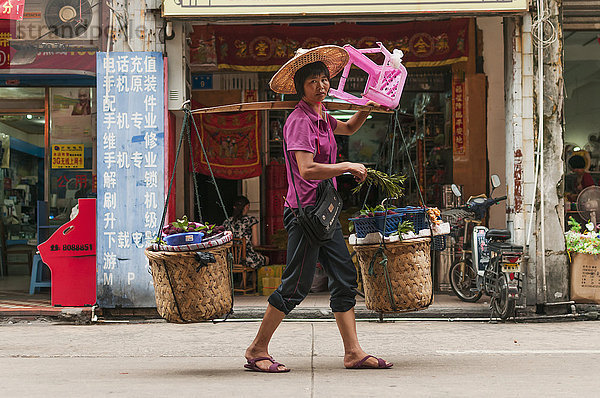 Eine Frau trägt ihre Einkäufe mit dem typischen Bambusstock  der in China sehr verbreitet ist; Xiamen  Provinz Fujian  China