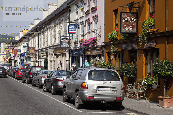 Eine Straße mit parkenden Autos und Einzelhandelsgeschäften; Kenmare  County Kerry  Irland