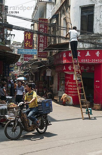 Mann benutzt eine Leiter auf gefährliche Weise in der Nähe der Straßendrähte  Xiamen lokaler Markt; Xiamen  Provinz Fujian  China