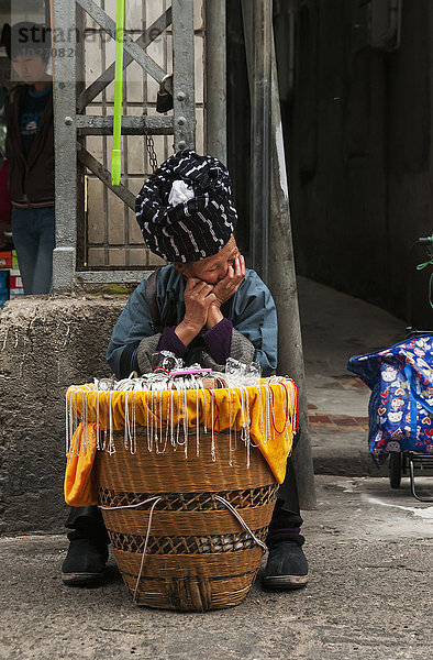 Eine ältere Frau aus einer ethnischen Minderheit  die auf dem Bashi-Markt Schmuck verkauft und an ihrem Tisch eingeschlafen ist; Xiamen  Provinz Fujian  China