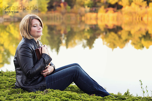 Reife christliche Frau umarmt ihre Bibel in einem Stadtpark an einem See im Herbst; Edmonton  Alberta  Kanada'.