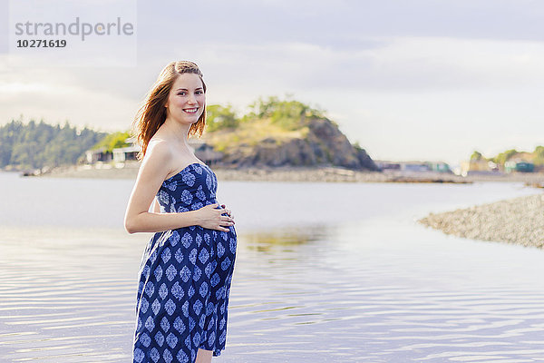 Eine junge Frau posiert mit einem Lächeln für ein Schwangerschaftsporträt an einem Strand am Meer; Nanaimo  British Columbia  Kanada'.