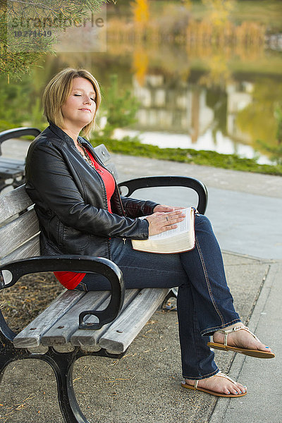 Reife christliche Frau studiert ihre Bibel in einem Stadtpark an einem See; Edmonton  Alberta  Kanada'.
