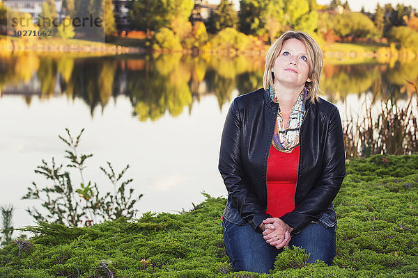 Ältere christliche Frau kniend und betend neben einem See im Herbst; Edmonton  Alberta  Kanada'.