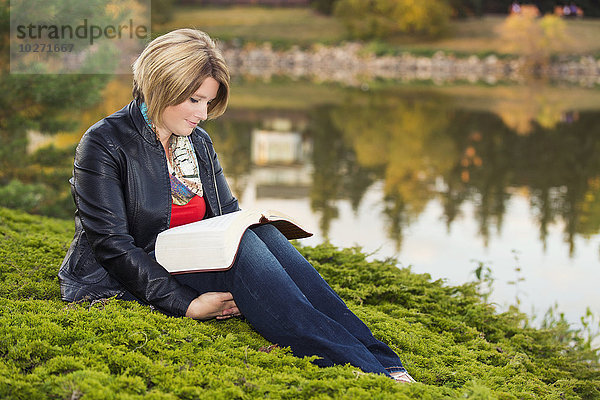 Ältere christliche Frau liest ihre Bibel in einem Park an einem See im Herbst; Edmonton  Alberta  Kanada'.