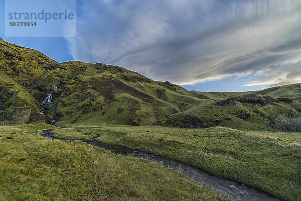 Linsenförmige Wolken bilden sich über einem Wasserfall und einem Bach  der in der Nähe von Vik zum Meer fließt; Island'.