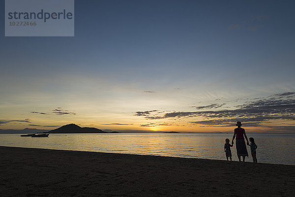 Silhouette einer Mutter mit einem Jungen und einem Mädchen am Strand von Cape Maclear bei Sonnenuntergang  Malawisee; Malawi'.