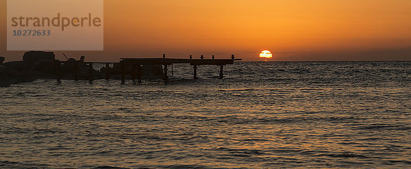 Die goldene Sonne versinkt hinter dem Wasser bei Sonnenuntergang mit orangefarbenem Himmel; Paphos  Zypern'.