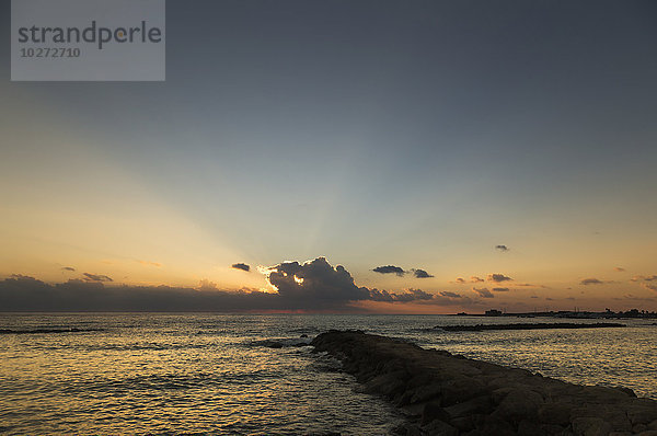 Wellenbrecher  der auf das Meer hinausführt  mit einem Sonnenuntergang über dem Wasser; Paphos  Zypern