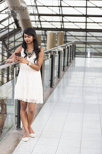 Junge Geschäftsfrau  die in einem Bürogebäude eine SMS auf ihrem Smartphone schreibt; Edmonton  Alberta  Kanada'.