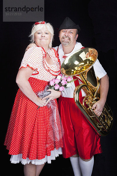 Stolzes  liebendes österreichisches Paar bei einer Talentshow in traditioneller bayerischer Kleidung mit Blumen und Tuba; Alberta  Kanada'.