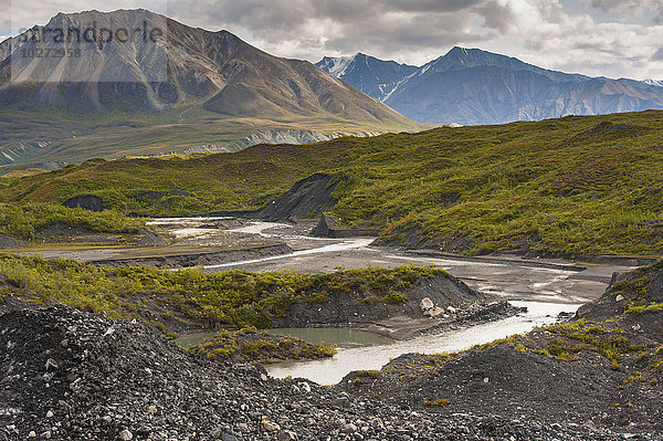 Thorofare River fließt neben dem mit Steinen und Pflanzen bedeckten Moldrow-Gletscher im Denali National Park and Preserve  Mount Eielson und die Alaska Range im Hintergrund; Alaska  Vereinigte Staaten von Amerika'.