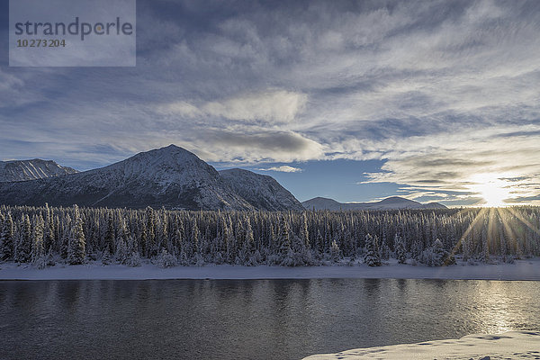 Die Sonne bricht an einem späten Winternachmittag durch die Wolken über dem Takhini River in der Nähe von Whitehorse  Yukon  Kanada.