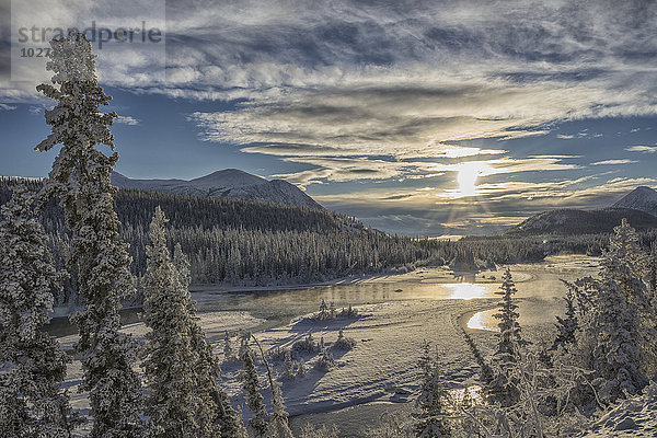 Die Sonne bricht an einem späten Winternachmittag durch die Wolken über dem Takhini River in der Nähe von Whitehorse  Yukon  Kanada.
