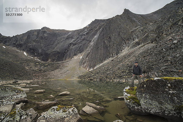 Mann steht auf einem Felsen neben einem unbenannten See in den Tombstone Mountains; Yukon Territory  Kanada'.