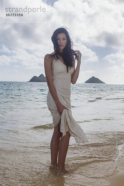 Junge Frau in weißem Kleid am Strand am Rande des Wassers; Kailua  Insel Hawaii  Hawaii  Vereinigte Staaten von Amerika'.
