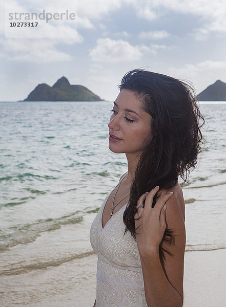 Junge Frau in weißem Kleid am Strand am Rande des Wassers; Kailua  Insel Hawaii  Hawaii  Vereinigte Staaten von Amerika'.