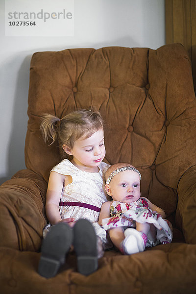 Ein junges Mädchen und ein kleines Mädchen sitzen auf der Couch und kuscheln  nachdem sie sich zum ersten Mal getroffen haben; Manhattan Beach  Kalifornien  Vereinigte Staaten von Amerika'.