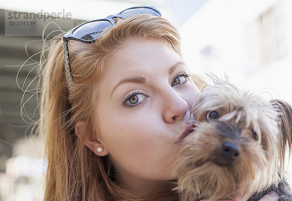 Rothaarige junge Frau hält und küsst ihren kleinen Hund; Vereinigte Staaten von Amerika'.