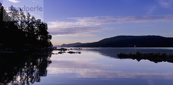 Küstenlinie  die sich bei Sonnenuntergang im Wasser spiegelt  mit Silhouette von Bäumen am Wasser; Mayne Island  British Columbia  Kanada'.