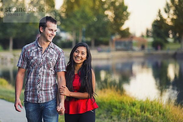Gemischtrassiges Paar  das Zeit miteinander verbringt und im Herbst um einen See in einem Park spaziert; St. Albert  Alberta  Kanada'.