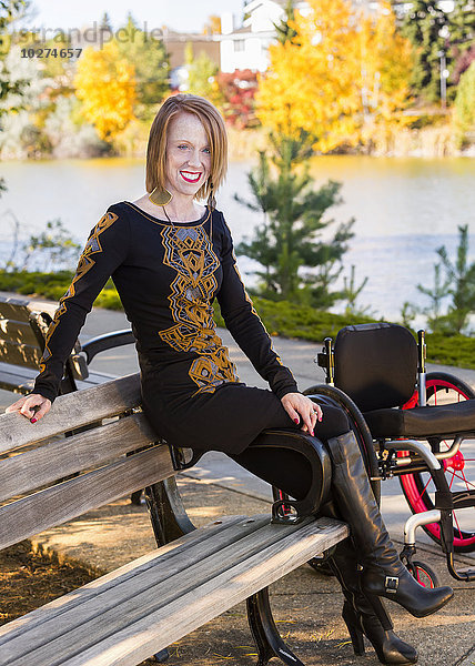 Junge behinderte Frau in ihrem Rollstuhl auf einer Bank in einem Stadtpark im Herbst; Edmonton  Alberta  Kanada